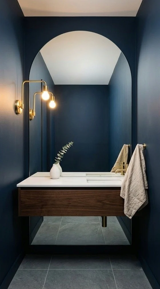 Deep navy walls with an oversized arched frameless mirror in a half bath