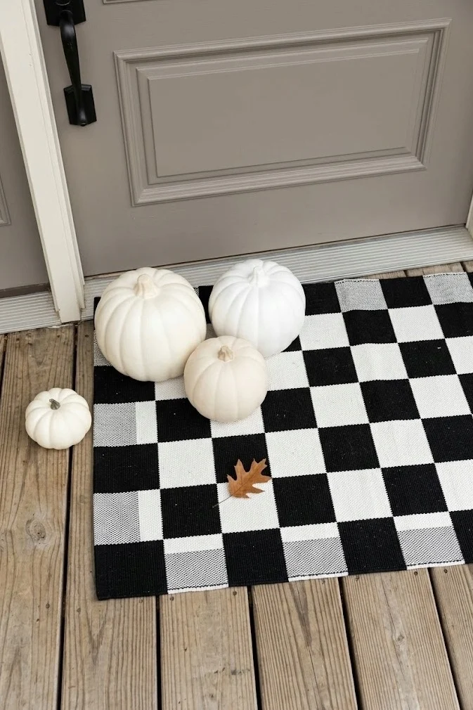 White pumpkins on a black-and-white checkerboard mat at a porch door