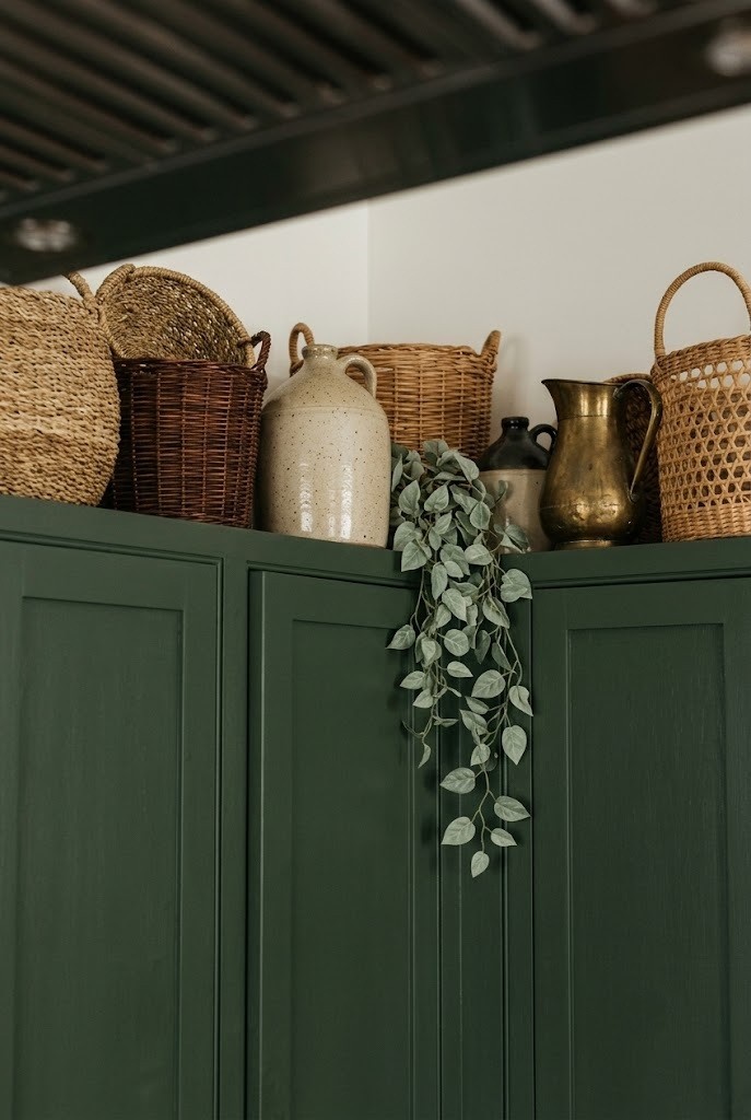 Woven baskets and jugs styled along the top of kitchen wall cabinets