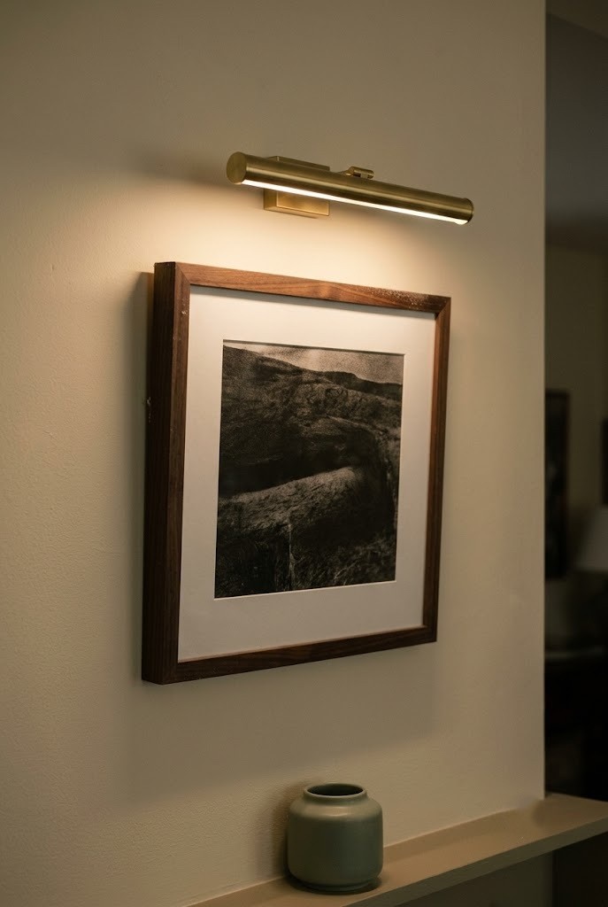 Slim brass picture light mounted above a framed print on an ivory wall