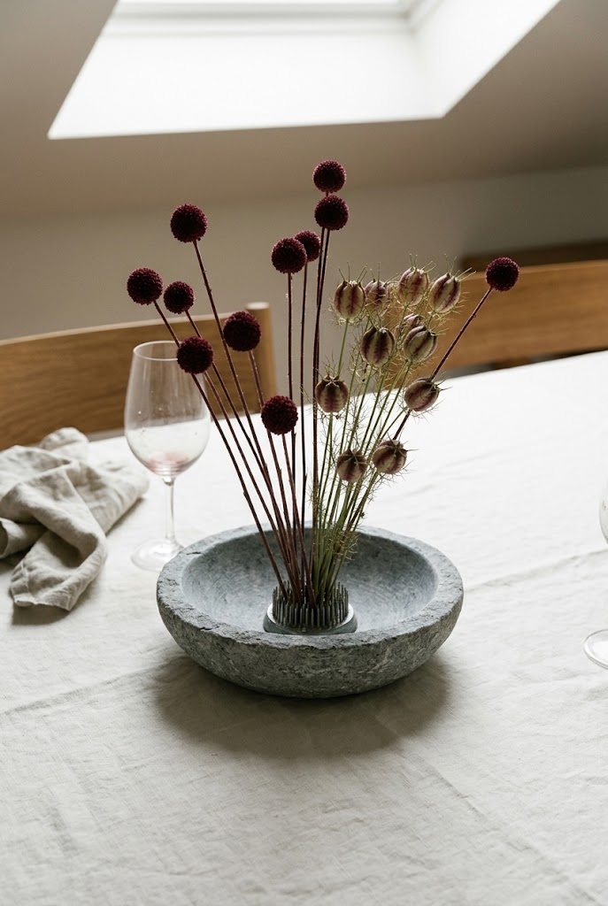 Burgundy craspedia and nigella pods in a shallow stone bowl, dried fall arrangement with no orange