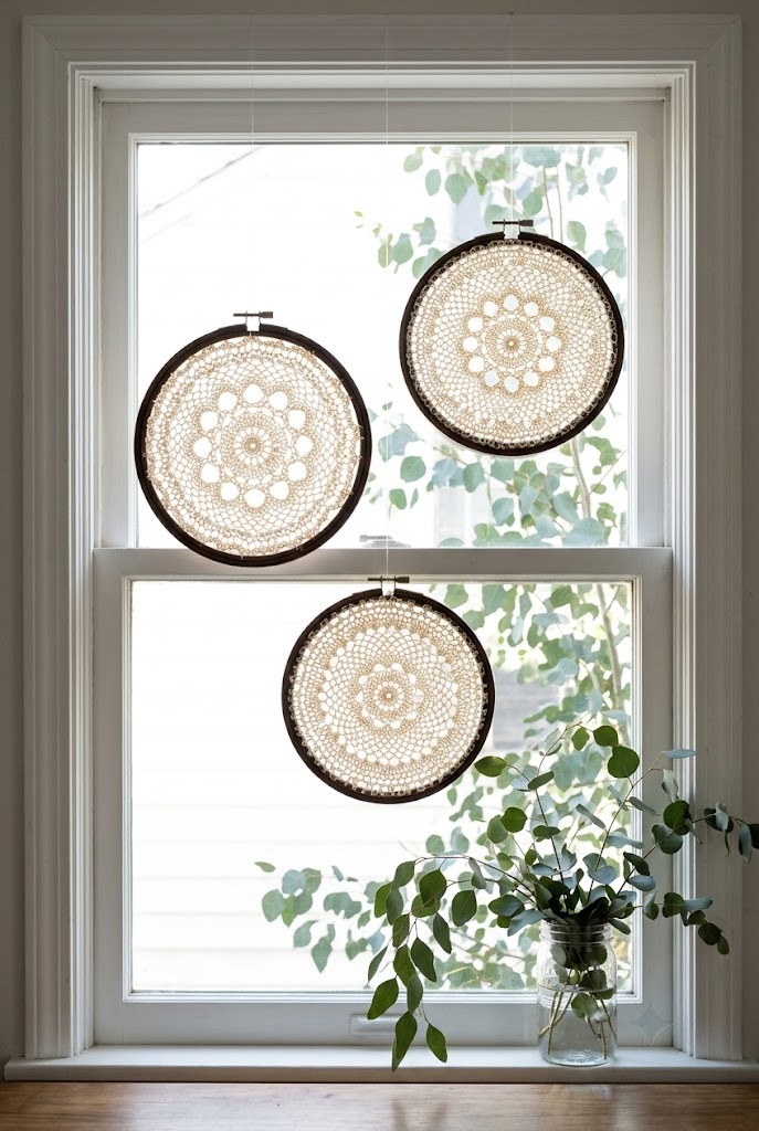 Three ivory doilies in dark walnut embroidery hoops hung at staggered heights in a window