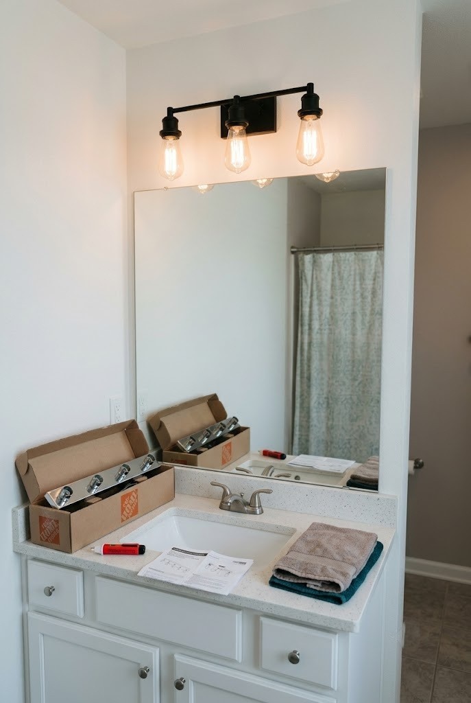 Matte black vanity light fixture replacing a builder light bar in a rental bathroom