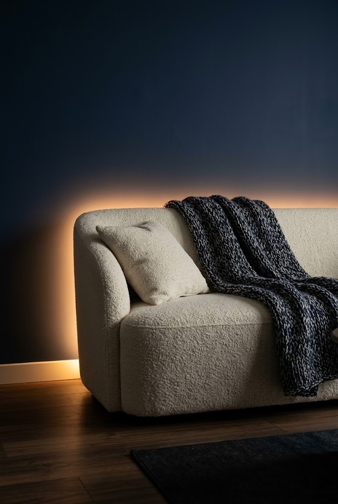 Hidden LED bar behind a sofa creating a warm backlit halo on the wall in a dim room