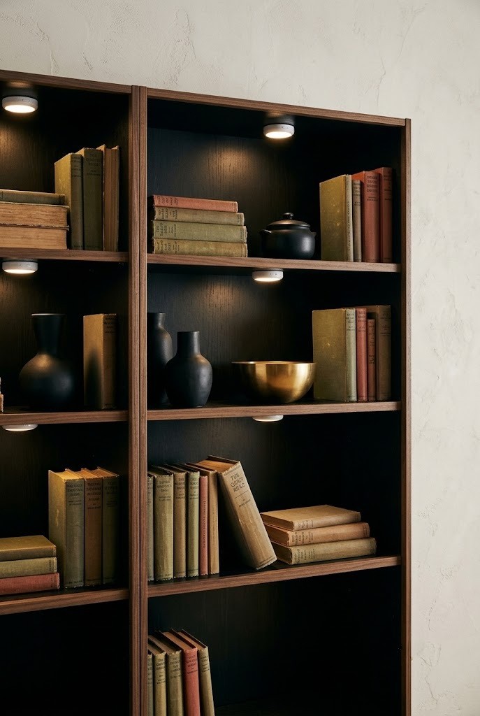 Battery puck lights glowing inside a dark bookcase with ceramics and books