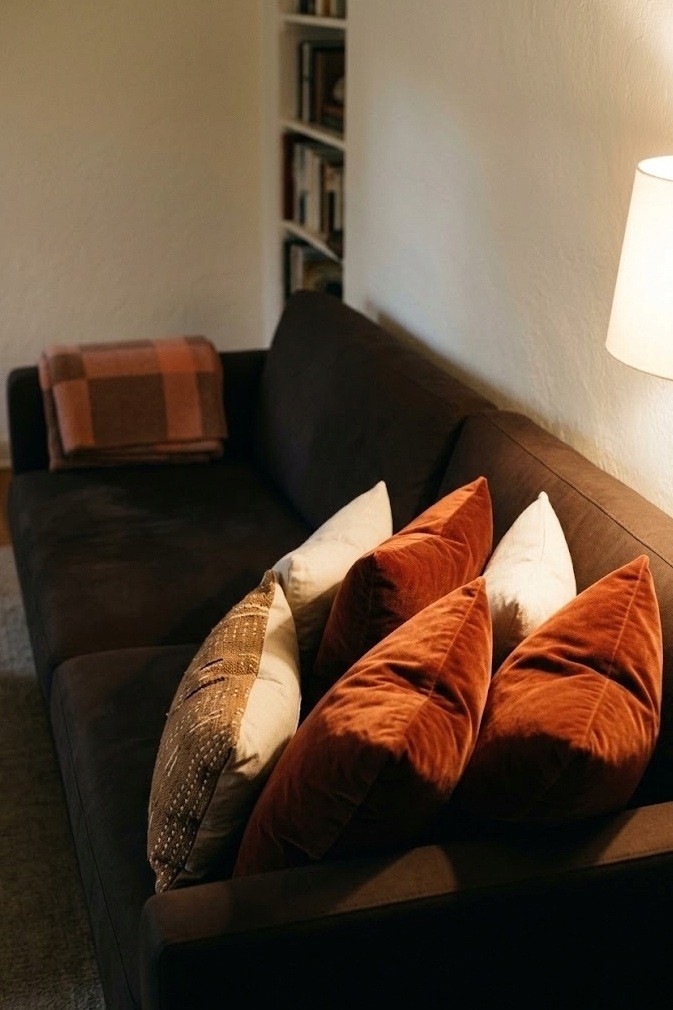 Rust velvet pillow covers clustered at one end of a chocolate brown sofa