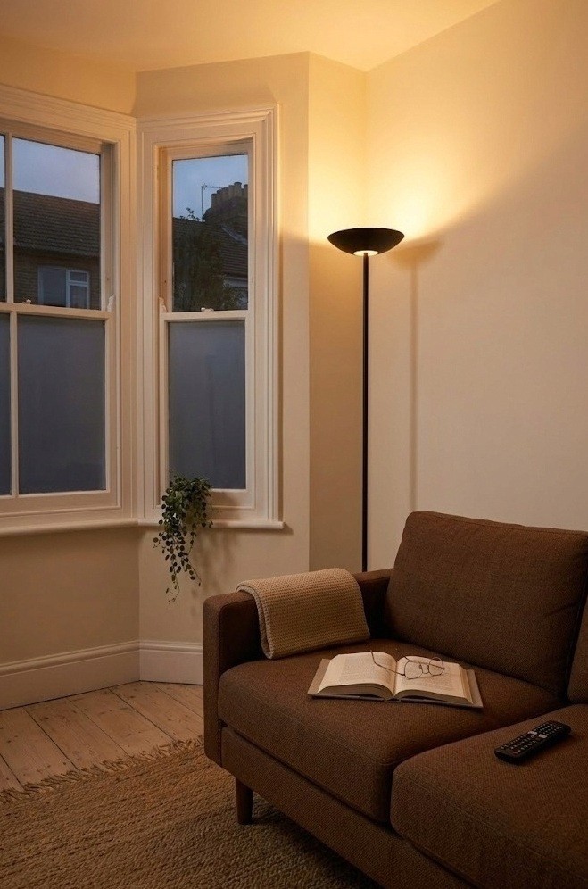 Slim floor lamp in the corner beside a brown sofa lighting a small living room warmly