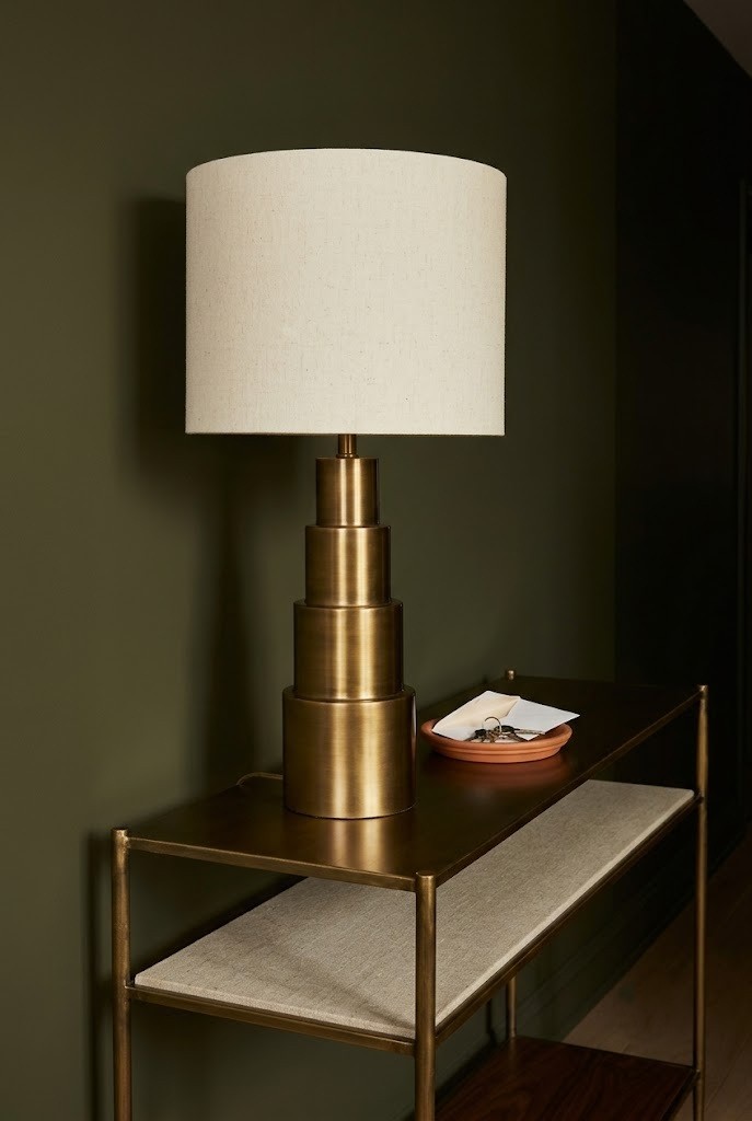Stepped brass table lamp with cream linen shade on a dark hallway console table