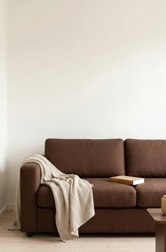 Brown sofa against a warm-white wall with an oatmeal throw over the arm in a small living room
