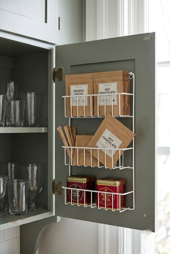 White wire rack on the inside of a cabinet door holding cocoa packets and stirrers